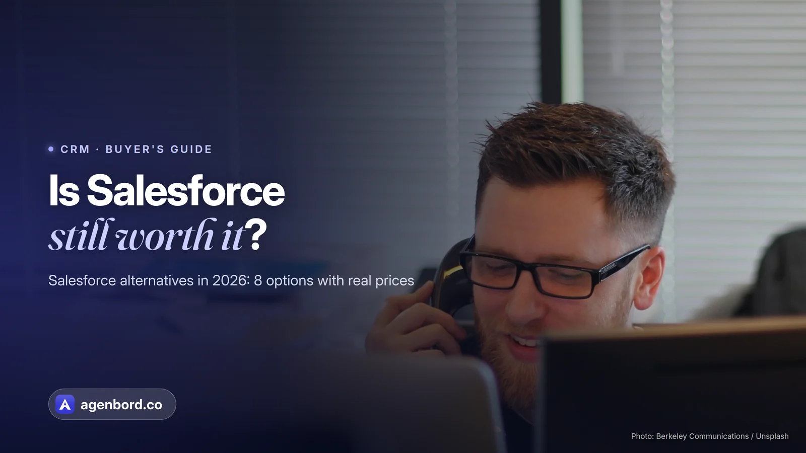 A man in glasses talks on a desk phone behind computer monitors in an office. Headline: Is Salesforce still worth it?