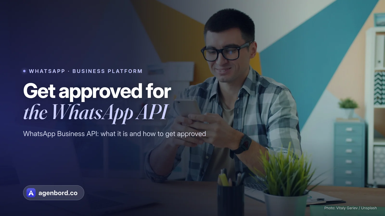 A man smiling at his phone at his desk. Headline: Get approved for the WhatsApp API
